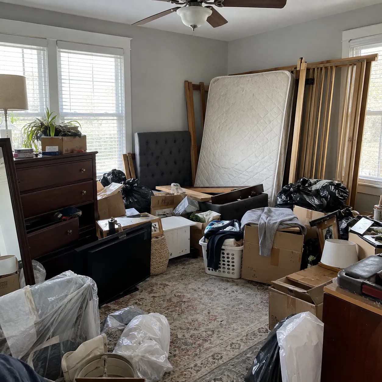 A Plano bedroom stacked with a mattress, dressers, bagged clothing and boxes before a cleanout