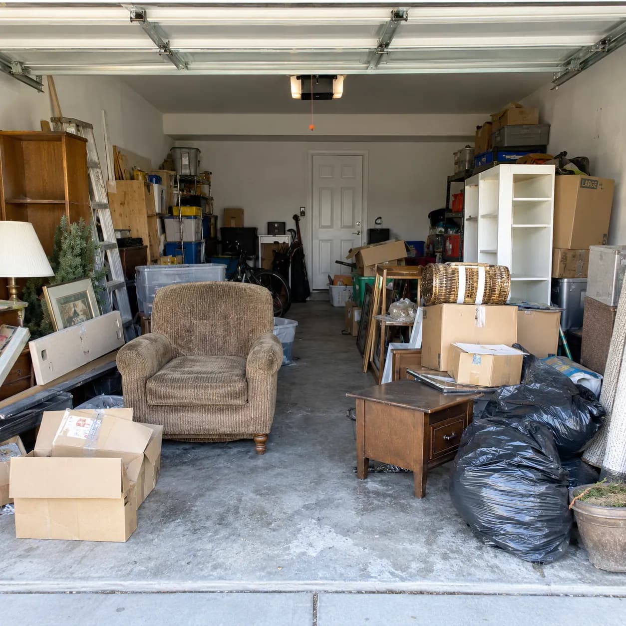 A two-car Plano garage packed with boxes, an armchair, shelving and bagged clutter before a cleanout