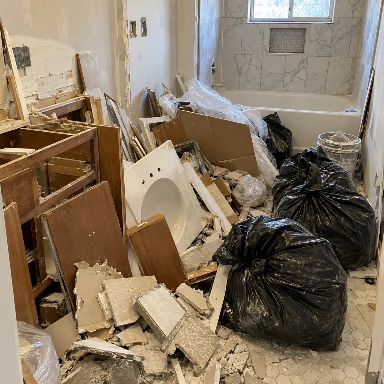 A demolished bathroom with an old sink, broken tile and vanity pieces stacked in the tub