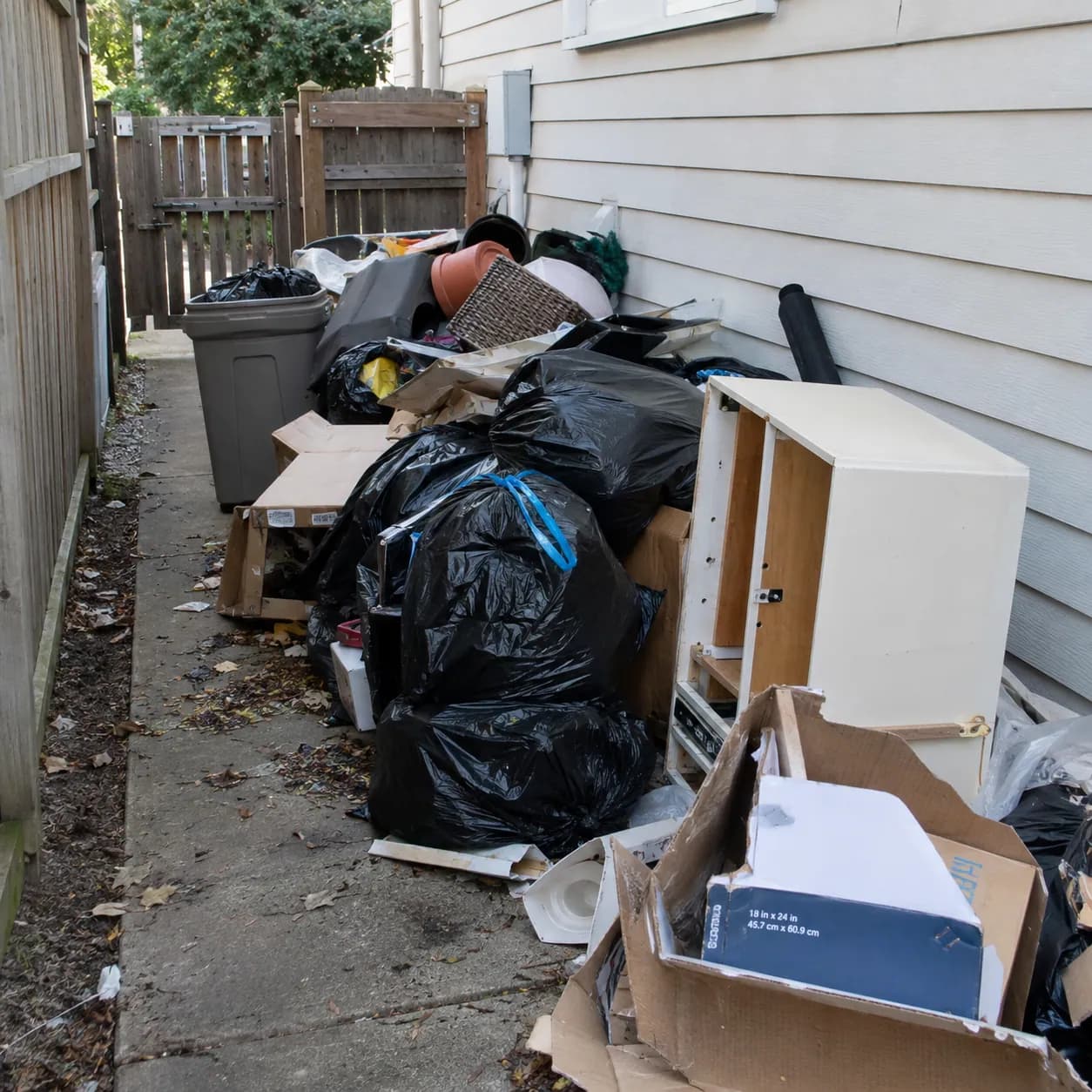 Household junk, bagged rubbish and broken furniture stacked along the side of a house