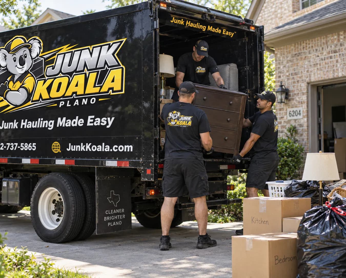 Junk Koala Plano crew lifting a wooden dresser into a truck marked A Cleaner, Brighter Plano